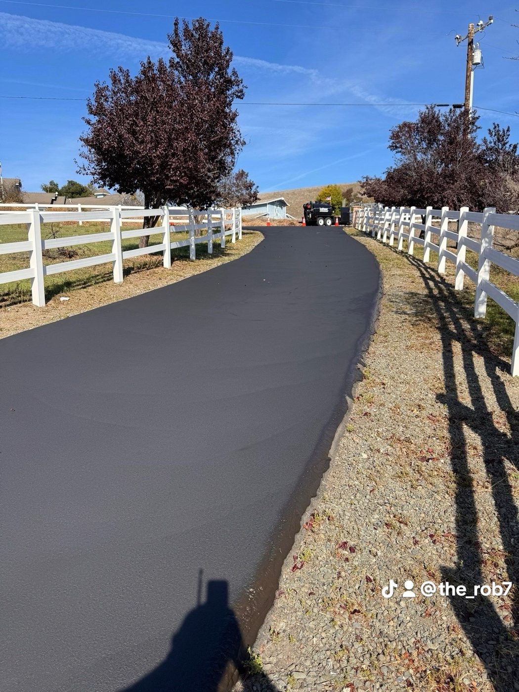 Long finished driveway between white fences